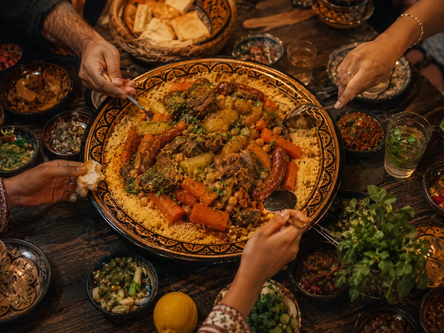 Des mains qui se tendent de tous les côtés vers un grand plat de couscous